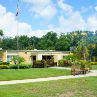 A small building with a flagpole in front, surrounded by grass and trees under a partly cloudy sky.