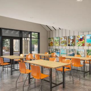 A modern cafe interior with orange chairs and wooden tables, featuring artwork on the walls.