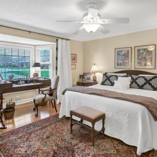 A cozy bedroom with a large bed and a study area by the window, featuring classic decor and warm lighting.