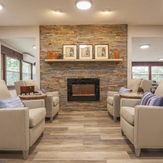 A cozy living room with a modern stone fireplace, flanked by comfortable beige armchairs on wooden flooring.