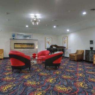 A modern lounge area featuring red chairs, a piano, and a colorful carpet.