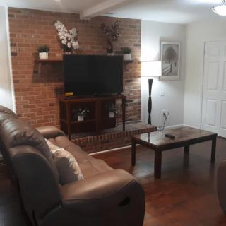 A cozy living room with a brick accent wall, featuring a TV and comfortable seating arrangement.