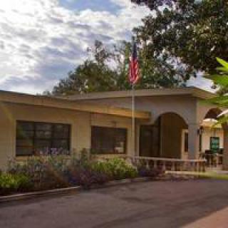 A small building with an American flag at the entrance, surrounded by trees and under a partly cloudy sky.