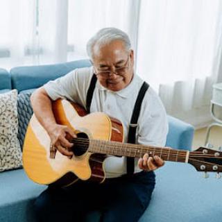 An elderly man sitting on a couch playing an acoustic guitar.