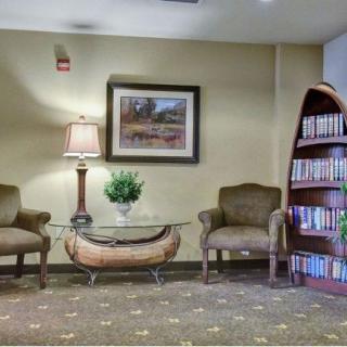 A cozy waiting area with two chairs, a glass top table, a lamp, and a bookshelf filled with books.