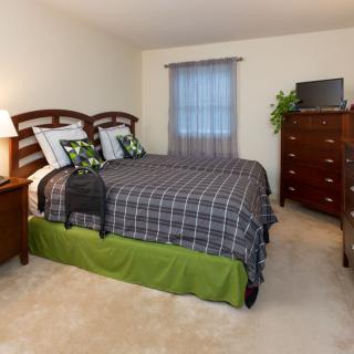 A cozy bedroom with a large bed, wooden furniture, and a window adorned with sheer curtains.