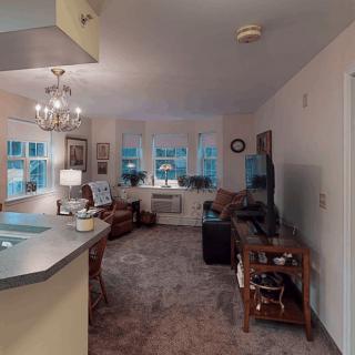 A cozy living room with a TV, sofa, and chandelier, adjacent to a kitchen counter.