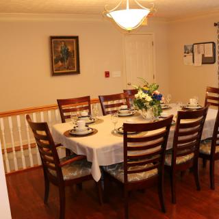 A dining room setup with a wooden table and chairs, adorned with a floral centerpiece under warm lighting.
