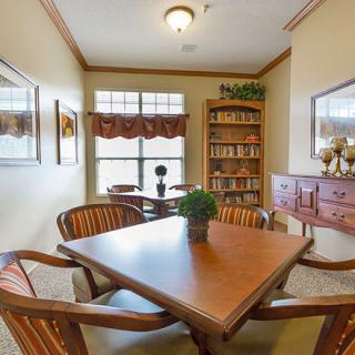 A cozy reading room with a table and chairs, surrounded by bookshelves and adorned with decor.