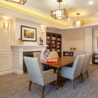 A cozy meeting room with a central table surrounded by chairs, featuring a fireplace and bookshelves.