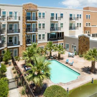 A modern apartment complex featuring a refreshing swimming pool surrounded by palm trees.