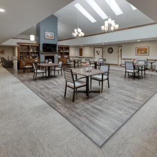 A spacious dining area with tables and chairs, featuring a central fireplace and overhead lighting under a vaulted ceiling.