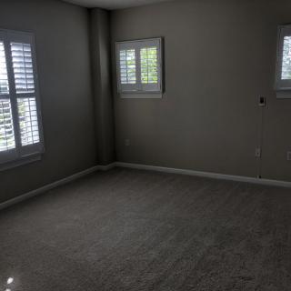 An empty room with carpeted floors and windows with blinds.