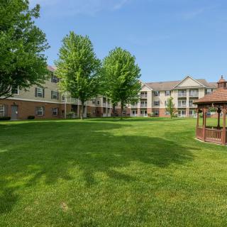 A peaceful residential apartment building with a well-maintained lawn and gazebo under a clear blue sky.