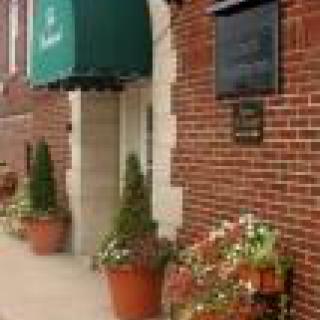 A building entrance with a green awning and potted plants, featuring a brick exterior.