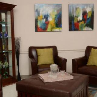 A cozy living room with leather chairs, colorful artwork, and a decorative cabinet.