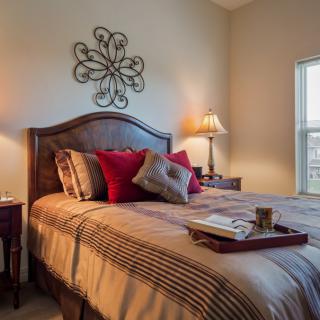 A cozy bedroom with a neatly made bed, decorative pillows, a bedside lamp, and a wall ornament.