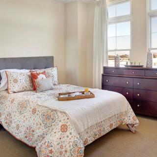 A cozy bedroom with a neatly made bed and a wooden dresser by the window.