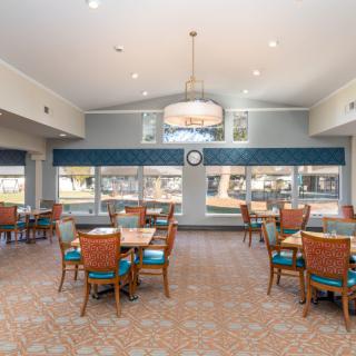 A spacious dining area with tables and chairs, featuring large windows and a chandelier.