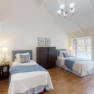 A bright bedroom with two twin beds, featuring wooden floors and a chandelier.