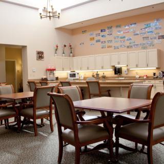 A spacious dining area with tables and chairs, featuring a well-equipped kitchen in the background.