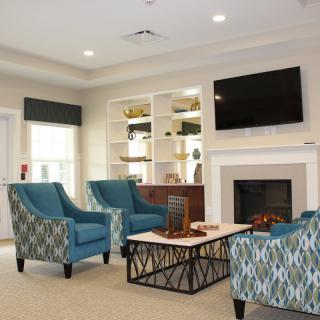 A cozy living room with blue patterned chairs, a fireplace, and a television mounted above it.