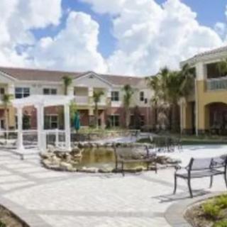 A courtyard with a pond, benches, and surrounding buildings under a partly cloudy sky.