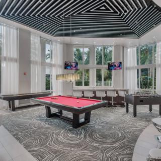 A modern game room featuring a pool table with bright natural lighting from large windows.