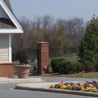 A roadside scene with a building, brick pillar, fence, and colorful flowers.