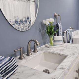A modern bathroom setup featuring a marble sink, elegant mirror, and decorative flowers.
