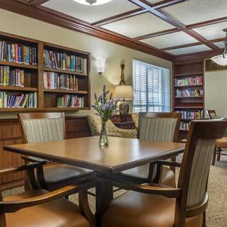 A cozy library reading room with bookshelves, a wooden table, and chairs.