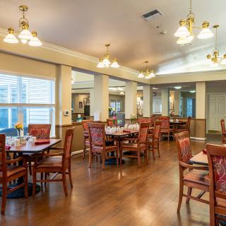 A spacious dining room with neatly arranged tables and chairs, warm lighting, and wood flooring.