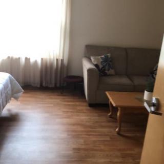 A cozy room with a bed, couch, and wooden flooring.