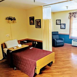 A tidy hospital room with a bed, side table, and a comfortable chair.