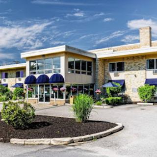 A welcoming hotel exterior featuring blue awnings and well-maintained landscaping under a bright sky.