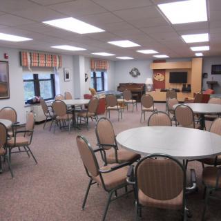 A spacious community room with multiple tables and chairs, well-lit with natural and artificial lighting.