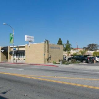A street view of a building with a clear blue sky in the background, featuring parked cars along the roadside.