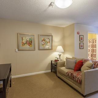 A cozy living room with a sofa, side table, lamp, and framed artwork on the walls.