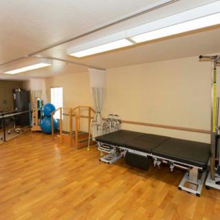 A spacious rehabilitation therapy room equipped with exercise balls, a treatment table, and parallel bars on a wooden floor.