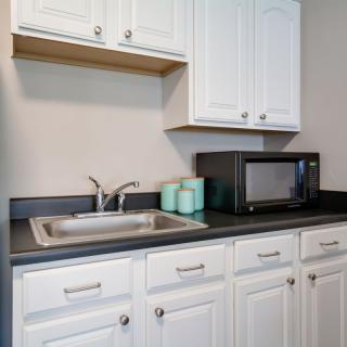 A small kitchen area with white cabinets, a sink, and a microwave on the countertop.