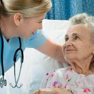 A nurse smiling and providing care to an elderly patient in a hospital setting.