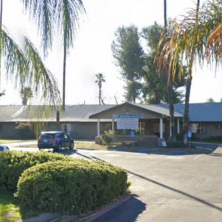 A single-story building surrounded by palm trees, with a car parked in the driveway.