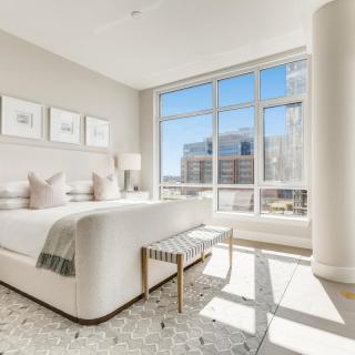 A modern, luxurious bedroom with large windows and a stunning city view, bathed in natural light.