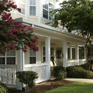 A charming house with a front porch surrounded by lush greenery and blooming flowers.