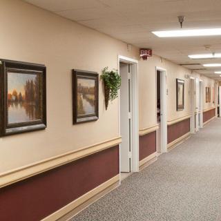 A long, brightly lit hallway with paintings on the walls and doors leading to rooms.