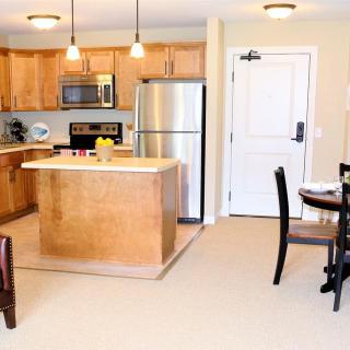 A modern kitchen with wood cabinets and stainless steel appliances, featuring an island and dining area.