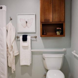 A modern bathroom with a toilet, towels, wall art, and a wooden cabinet.