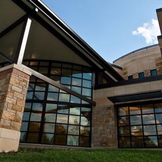 A modern building with large glass windows and a stone facade against a blue sky with clouds.