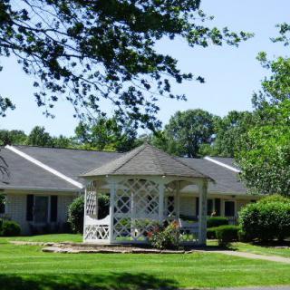 A charming gazebo on a well-maintained lawn in front of a house surrounded by trees.