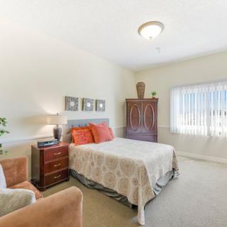 A bright and cozy bedroom with a bed, armchair, wardrobe, and lamp.